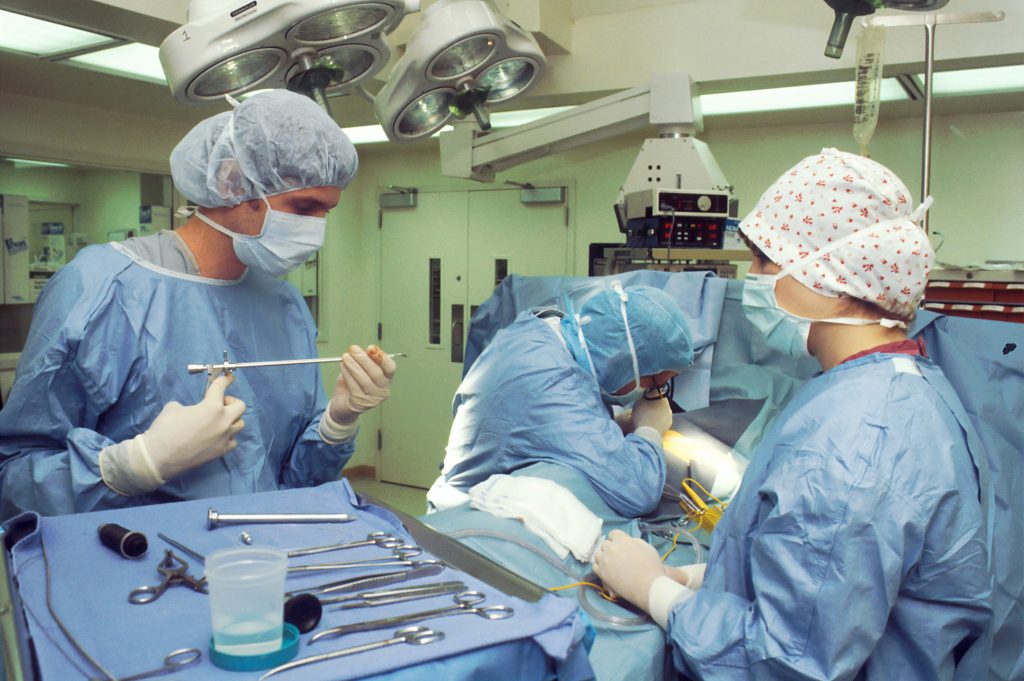 Three doctors in blue scrubs performing surgery in an operating theatre